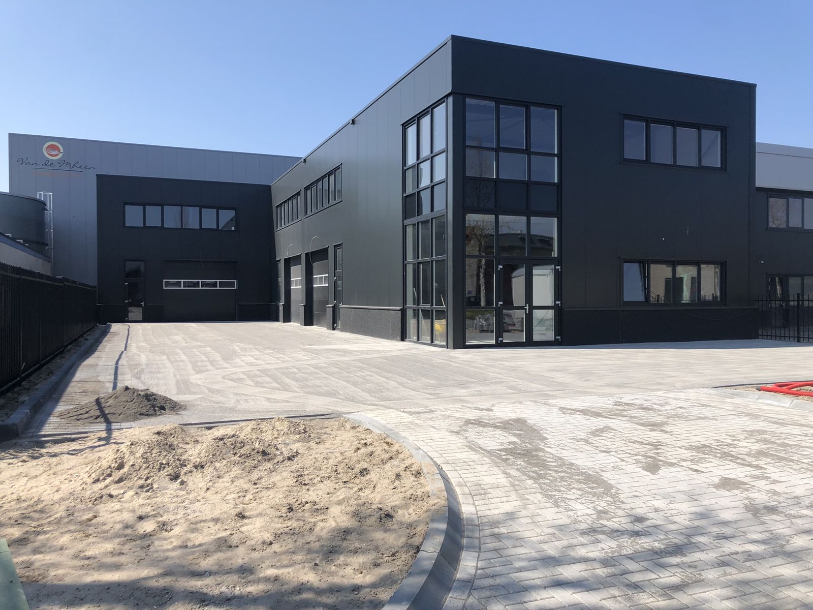Nieuw gelegde grijze bestrating met gebogen trottoirband voor een modern zwart bedrijfspand