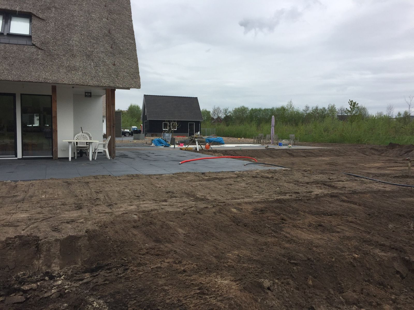 Afgegraven en geëgaliseerde grond achter een woning met rieten kap, klaar voor verdere aanleg
