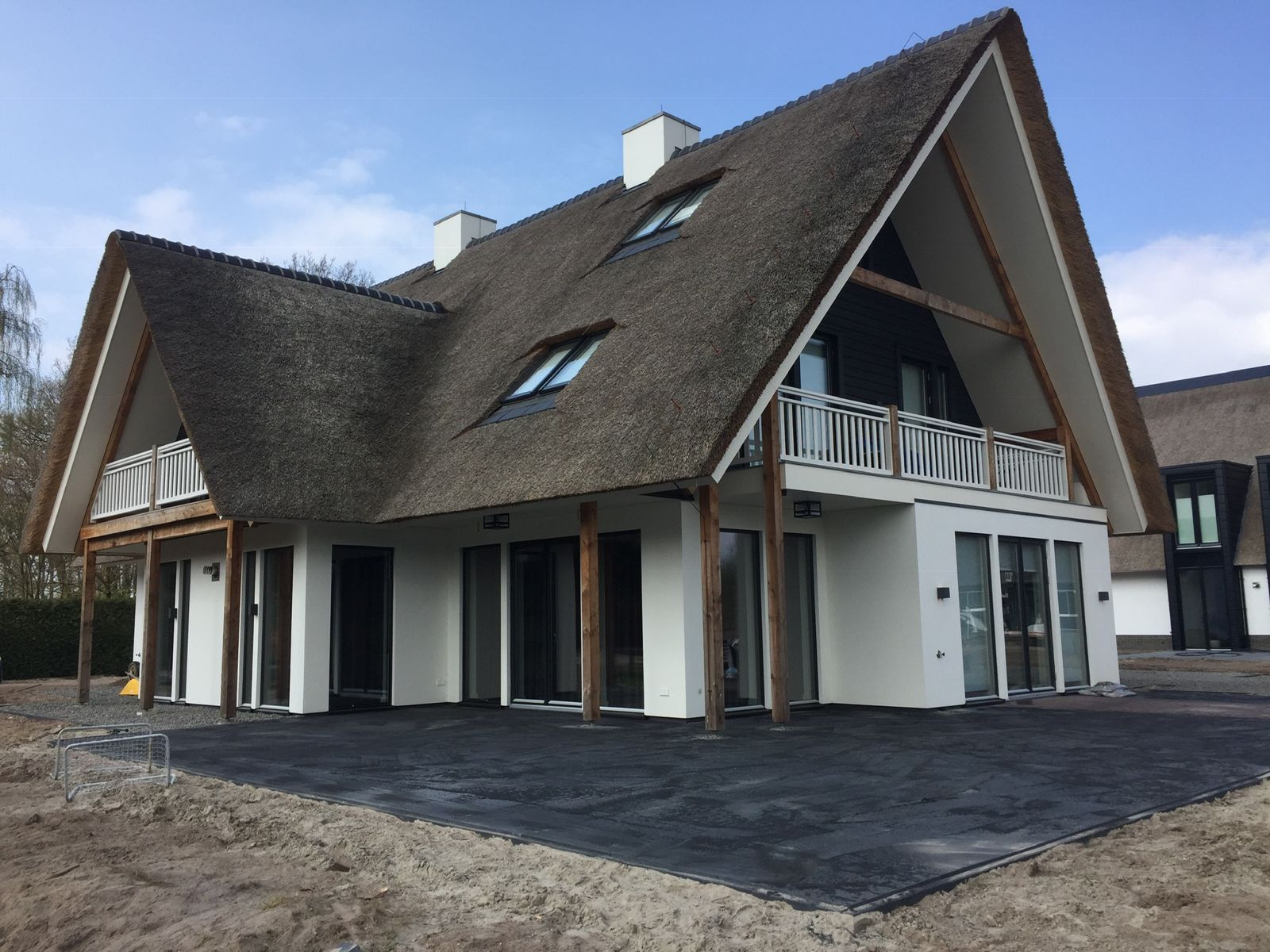 Vrijstaande woning met rieten kap en balkon, met nieuw gelegde donkere bestrating rondom